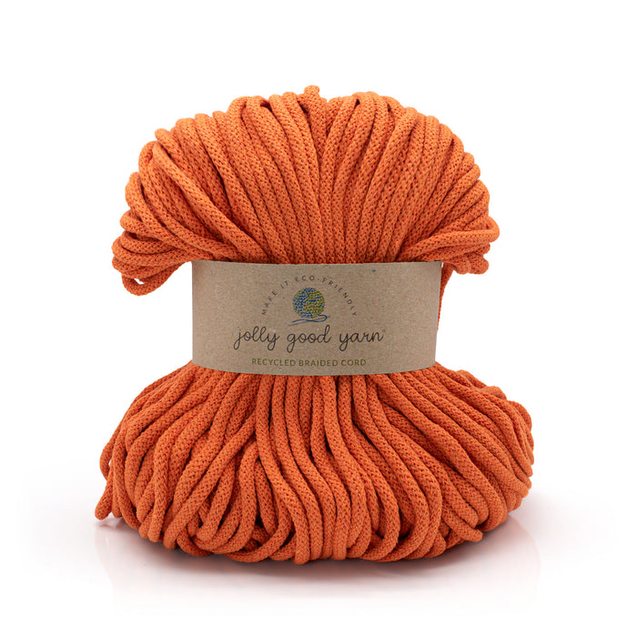 A skein of Jolly Good Yarn recycled braided cord in a vibrant orange color, wrapped in a brown paper label, on a clean white background.