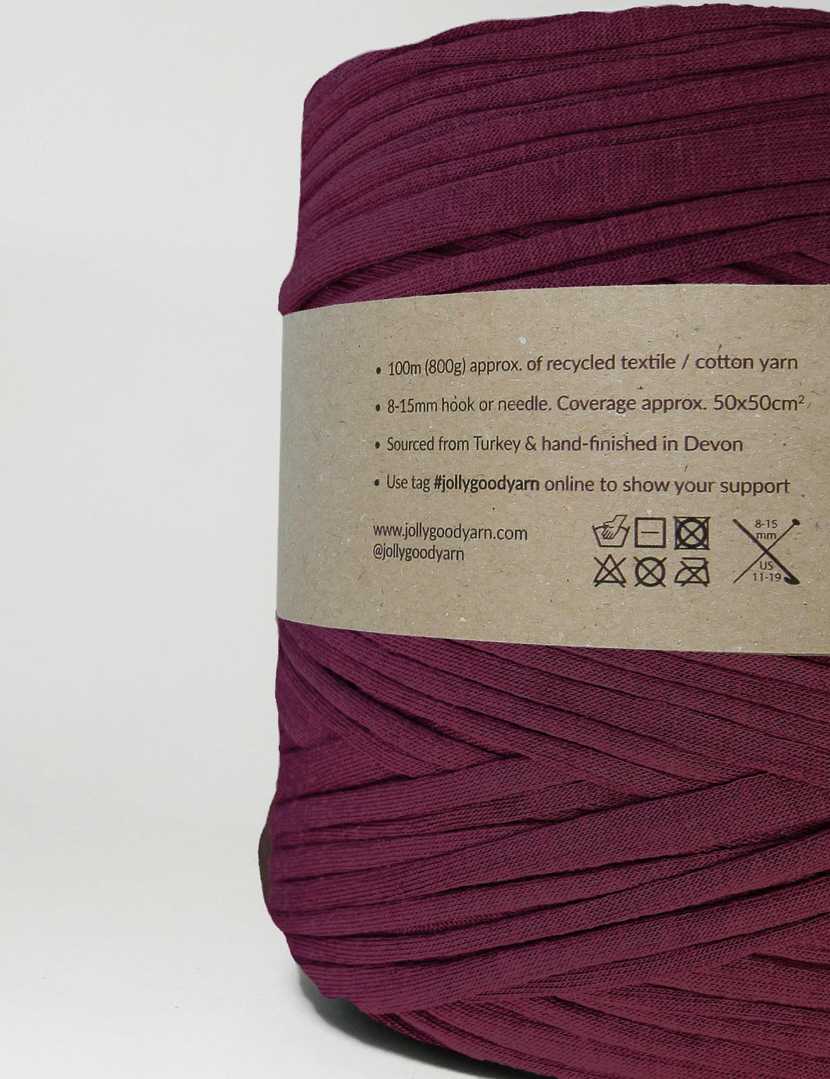 A close-up of a spool of deep plum purple knit yarn with a brown paper label showing product details, set against a plain white background.